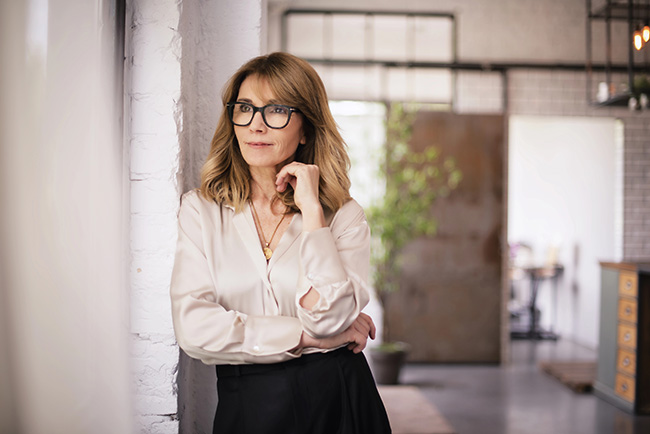 Woman standing thoughtfully in a modern workspace, symbolizing reinvention and life's changing stages.