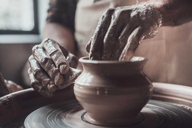 Hands shaping a clay pot on a pottery wheel
