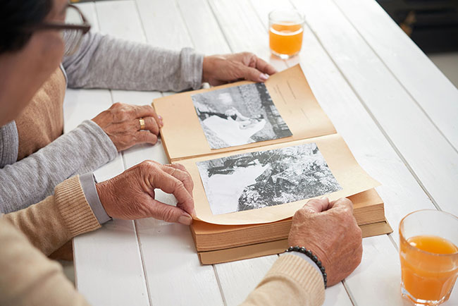 Two older adults looking through a family photo album with black-and-white photographs.