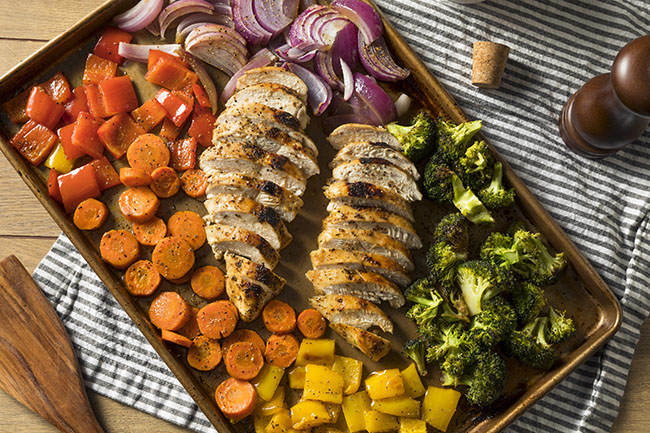 Sheet pan supper with roasted chicken, carrots, broccoli, and red onions.